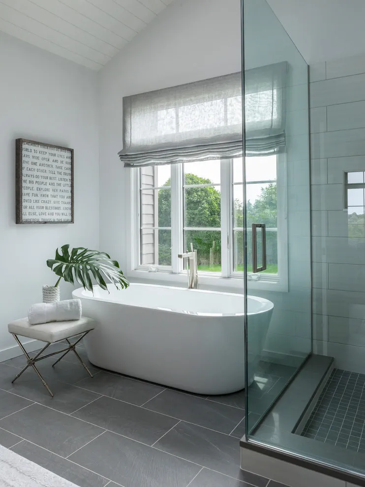 Gray rectangular floor tiles sit below a white bath beside a large window
