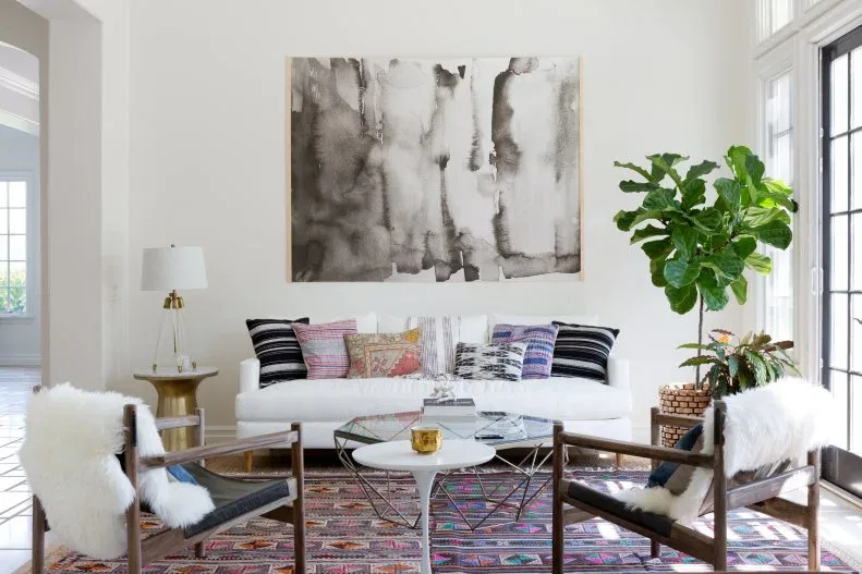 White sofa and two dark wooden armchairs around round tables beneath a large abstract picture.