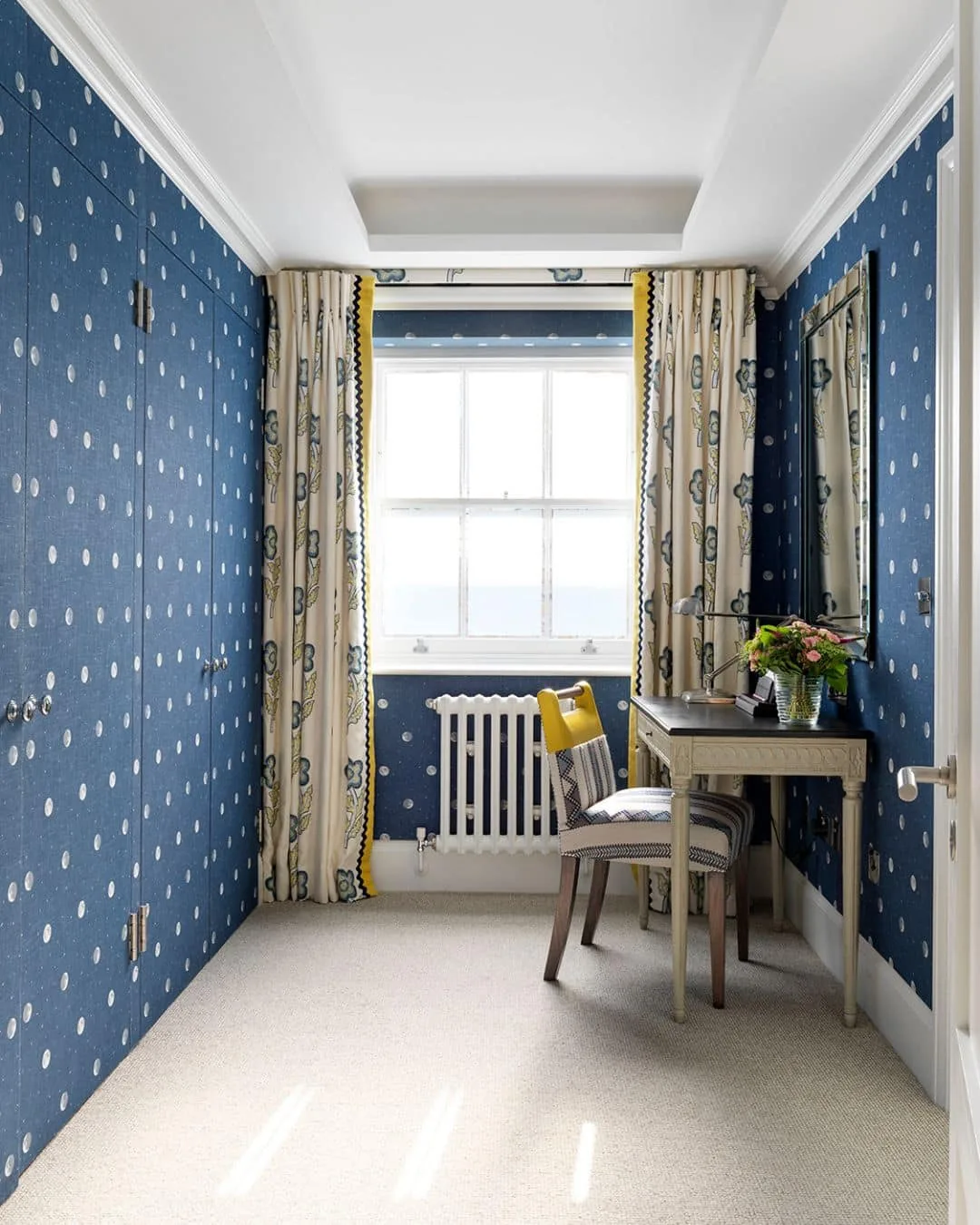 Narrow dressing area with blue moon-and-star patterned walls, a window, desk and chair.