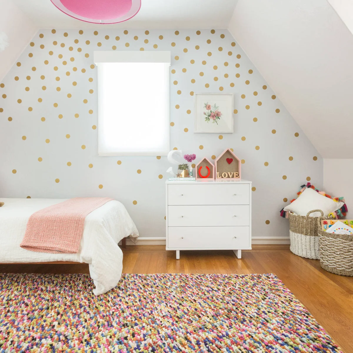 Small bedroom under a sloping ceiling with pale pink walls, a white bed, pink throw and multicolored rug