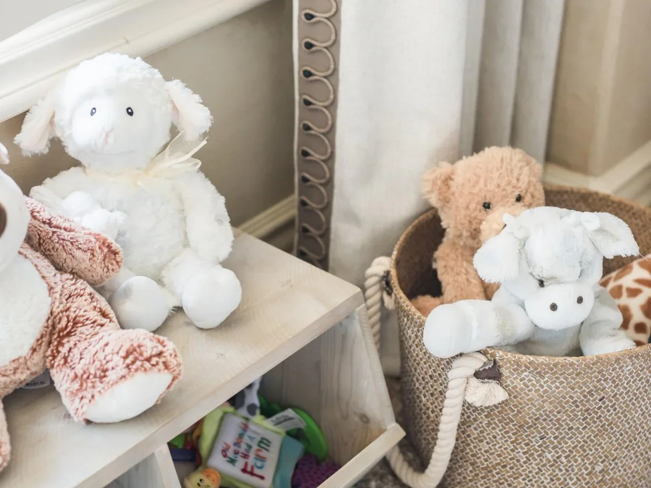 A woven basket holds plush animals beside a low storage unit with toys in its cubbies.