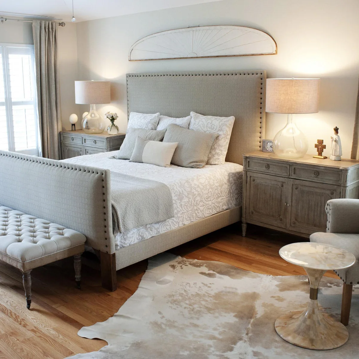 Pale tufted bench in front of a tall upholstered footboard with nailhead trim