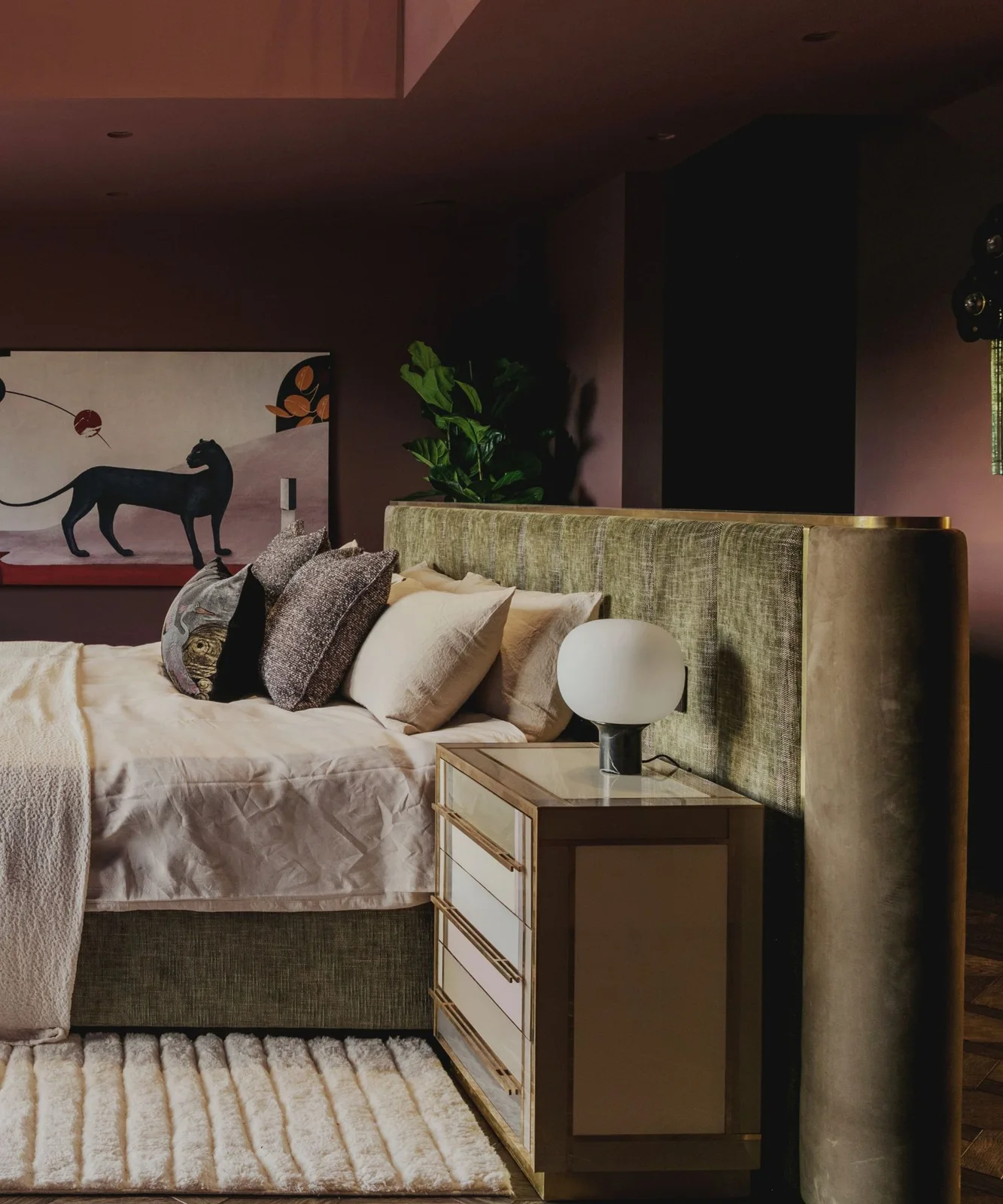 Burgundy walls surround a broad pale green headboard beneath a framed black-panther picture beside a gold-edged cabinet and round white lamp