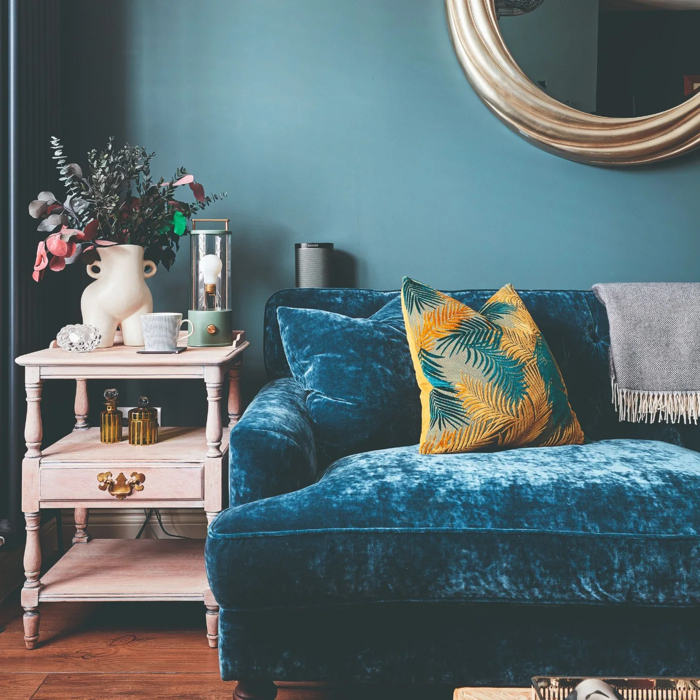 A deep blue sofa sits beside a pale pink side table with a drawer and open shelves against a blue wall.