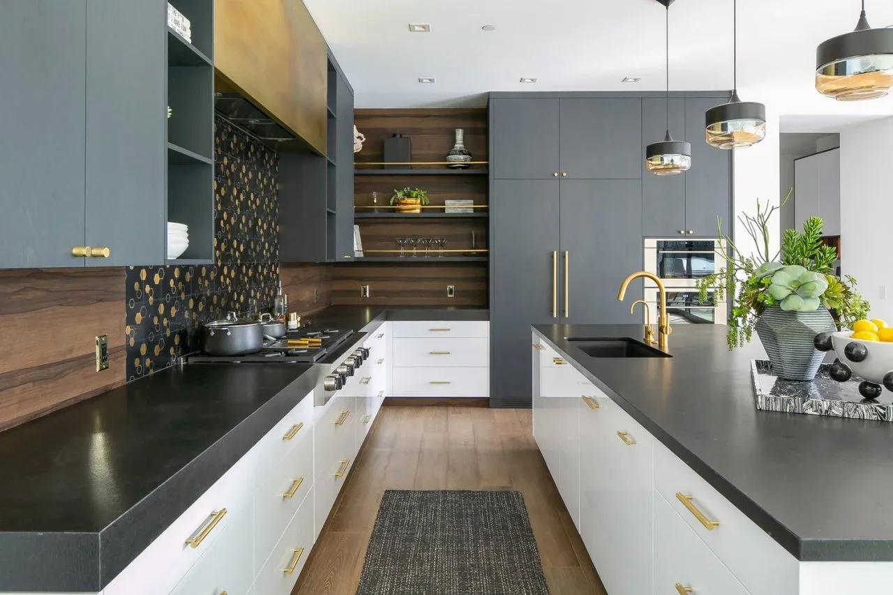 Gray upper and tall cabinets contrast with white lower drawers, dark counters and a warm wood-look backsplash in a modern kitchen.