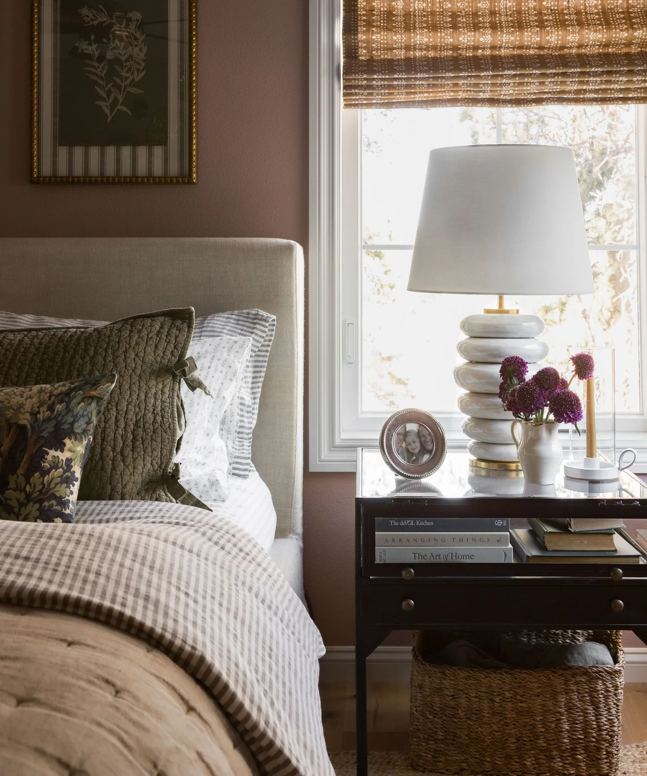 Dusty rose bedroom wall beside white window trim, olive cushions and checked bedding.