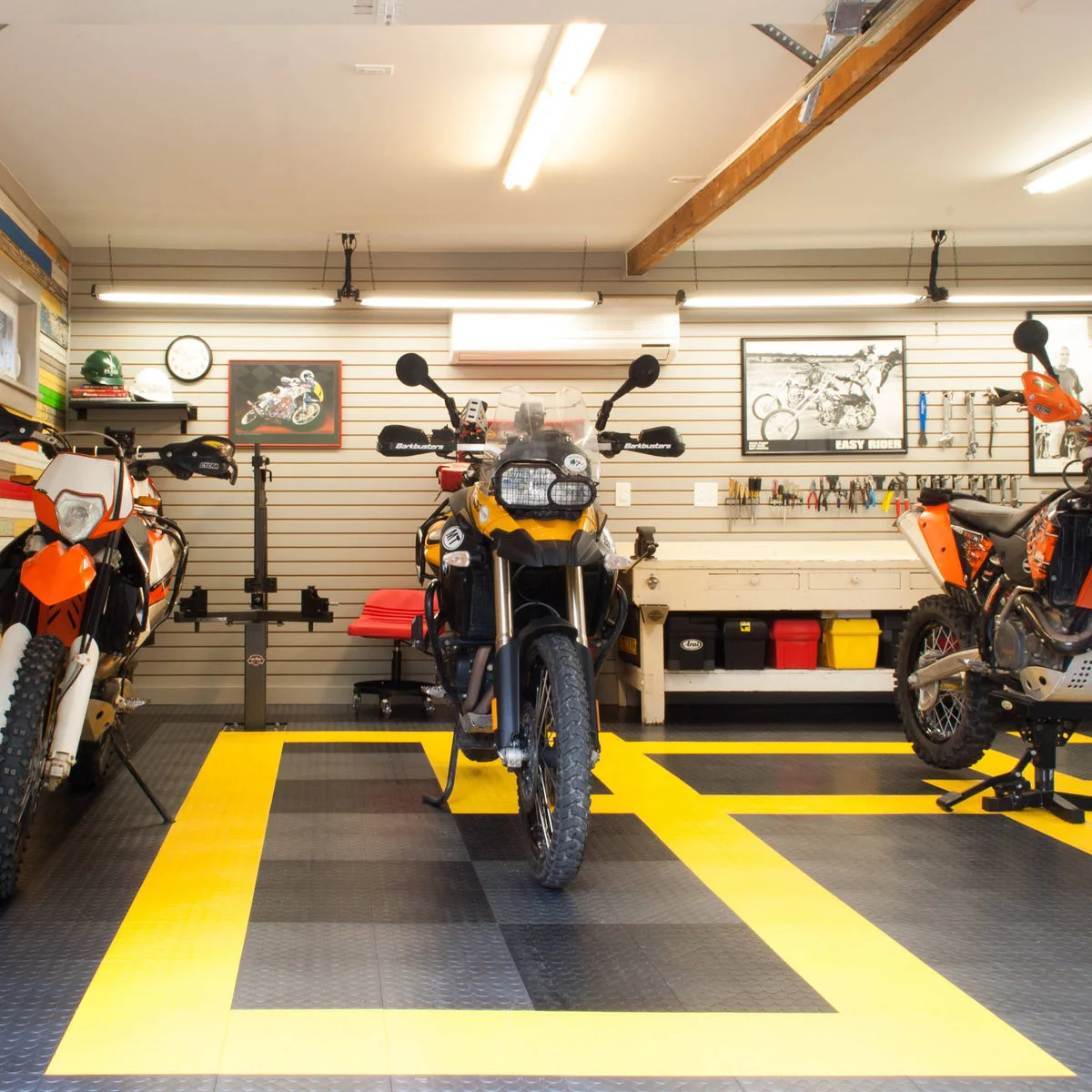 Motorcycle garage with bright yellow floor outlines, a white workbench and tools hanging on a slat wall.