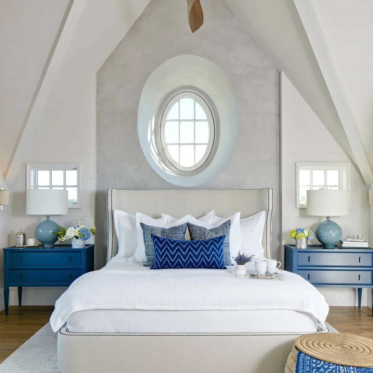 Blue two-drawer bedside chests with matching lamps beneath a round attic window