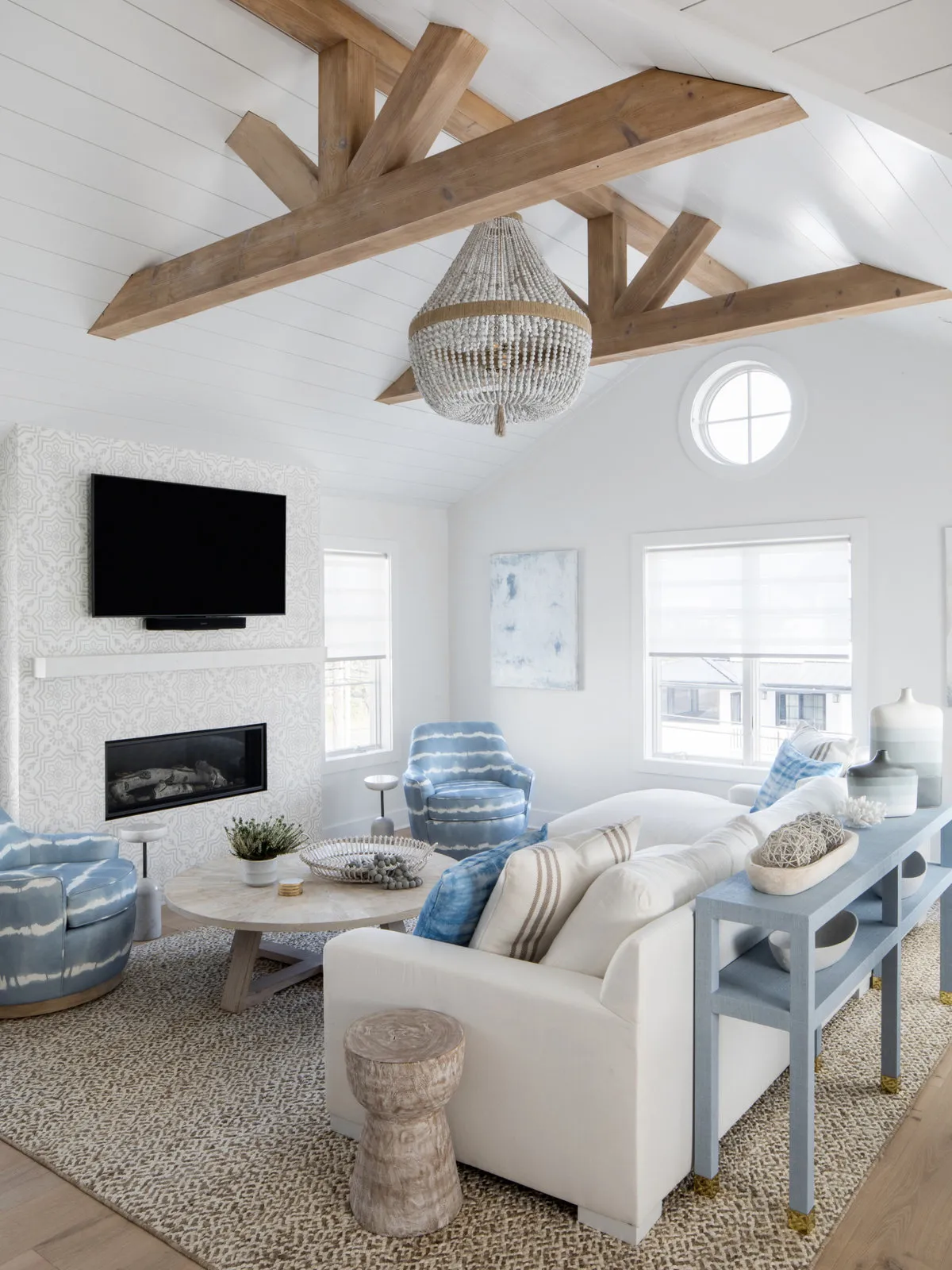 Light seating sits beneath exposed timber beams near a dark fireplace and pale walls.