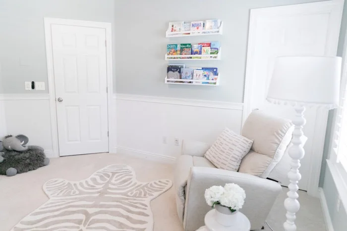 A pale zebra-shaped patterned rug lies beside a cream nursery chair beneath wall-mounted book ledges.