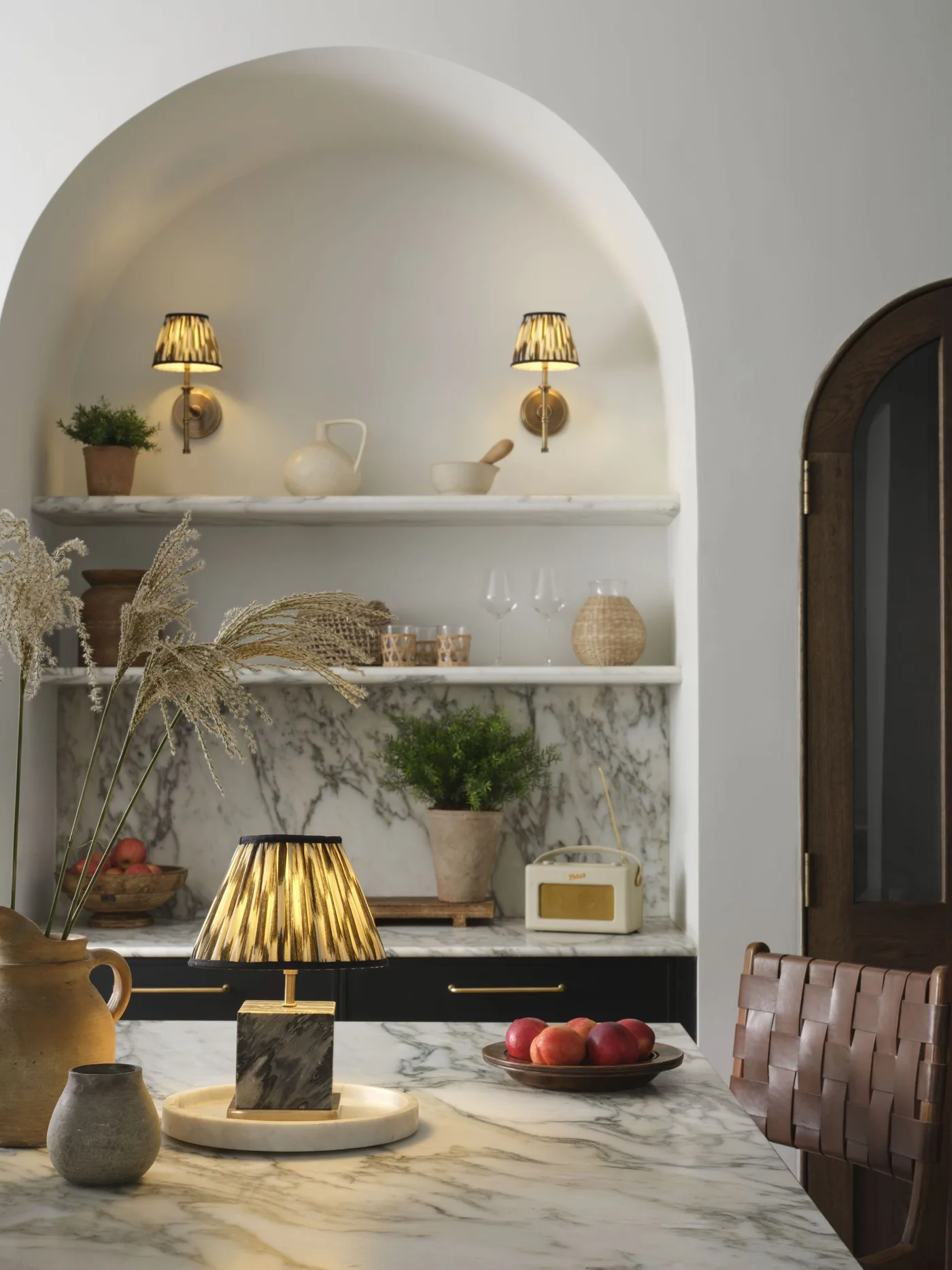 Small pleated lamp on a veined dining table with matching pleated wall lights in an arched alcove