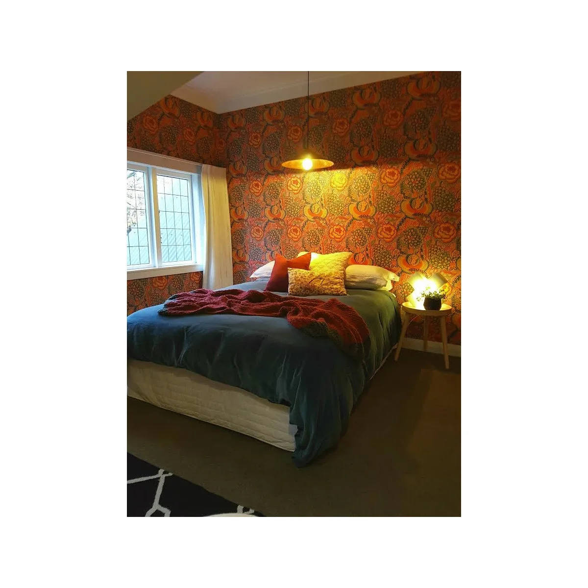 Teen bedroom with an orange patterned wall, dark teal bedding and a red textured throw