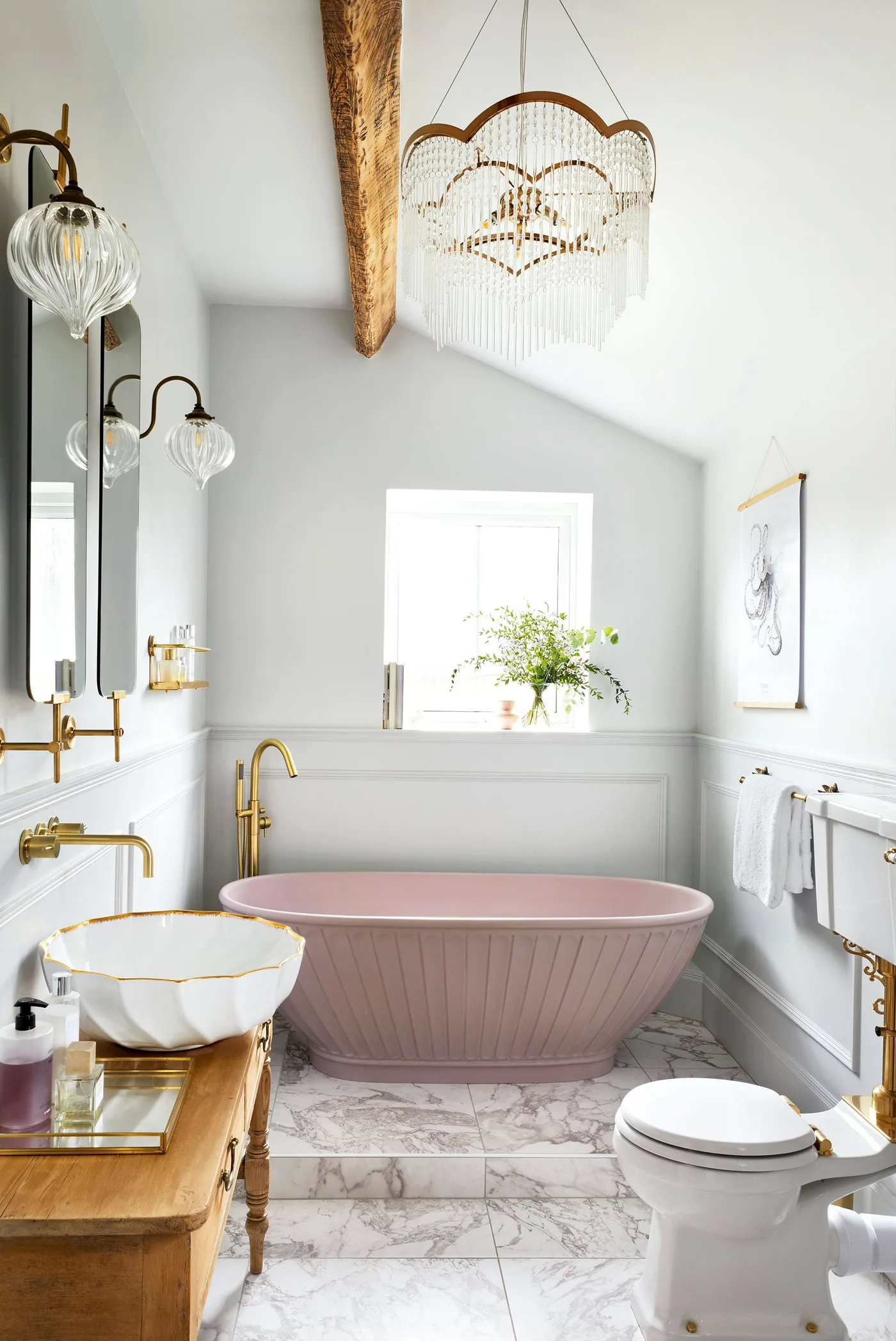 Pale pink fluted tub in a light bathroom with paneled walls, warm metal taps and an exposed ceiling beam.