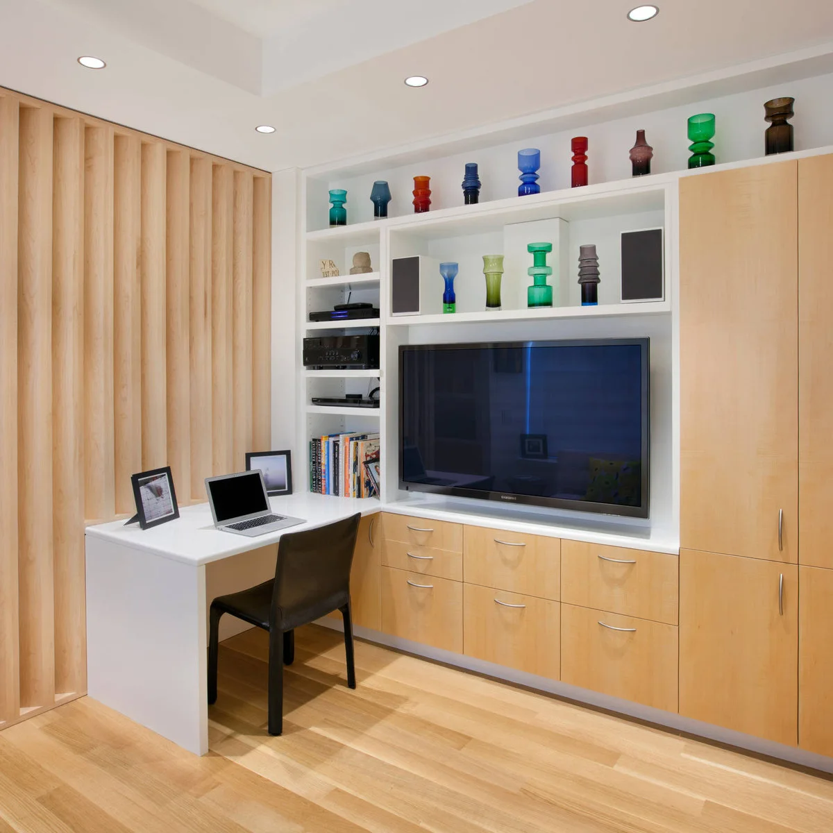 Compact room with television above wood drawers, side cabinets and a white desk at one end