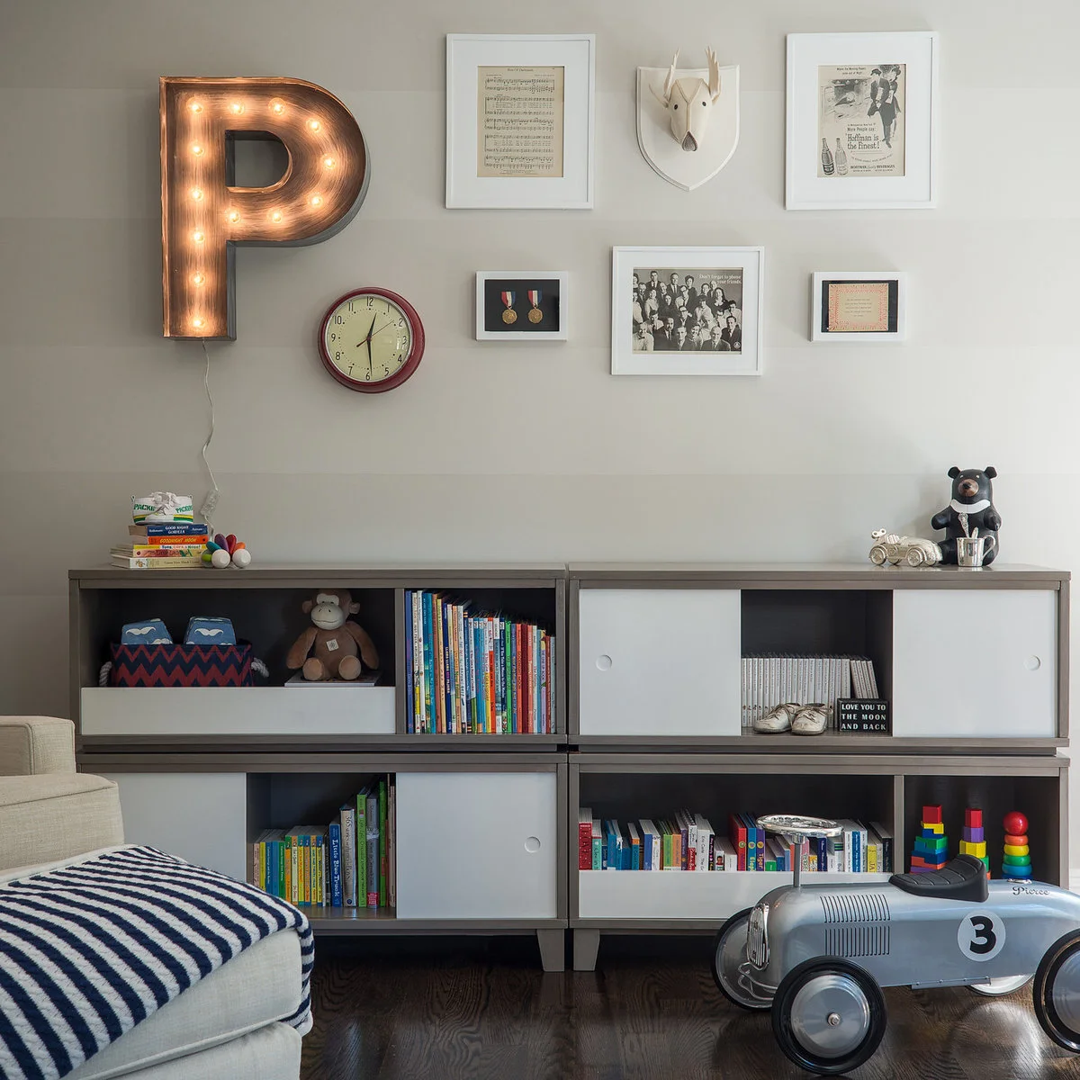 Low nursery storage units with sliding white fronts, colorful books and a family picture display above