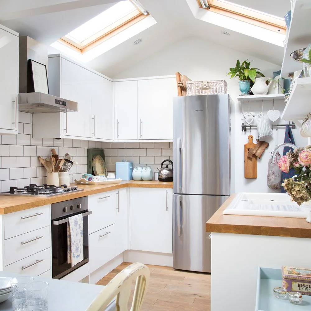 White flat-front cabinets and wood counters form a compact kitchen beneath two roof windows and a sloping ceiling.
