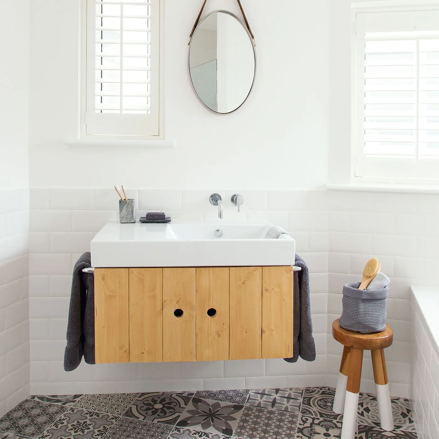 Floating wooden vanity with towels on side rails and a basket on a stool
