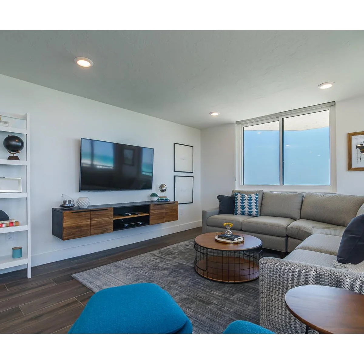 A floating wood-front media cabinet has an open center section beneath a television, with small accessories grouped at the ends.