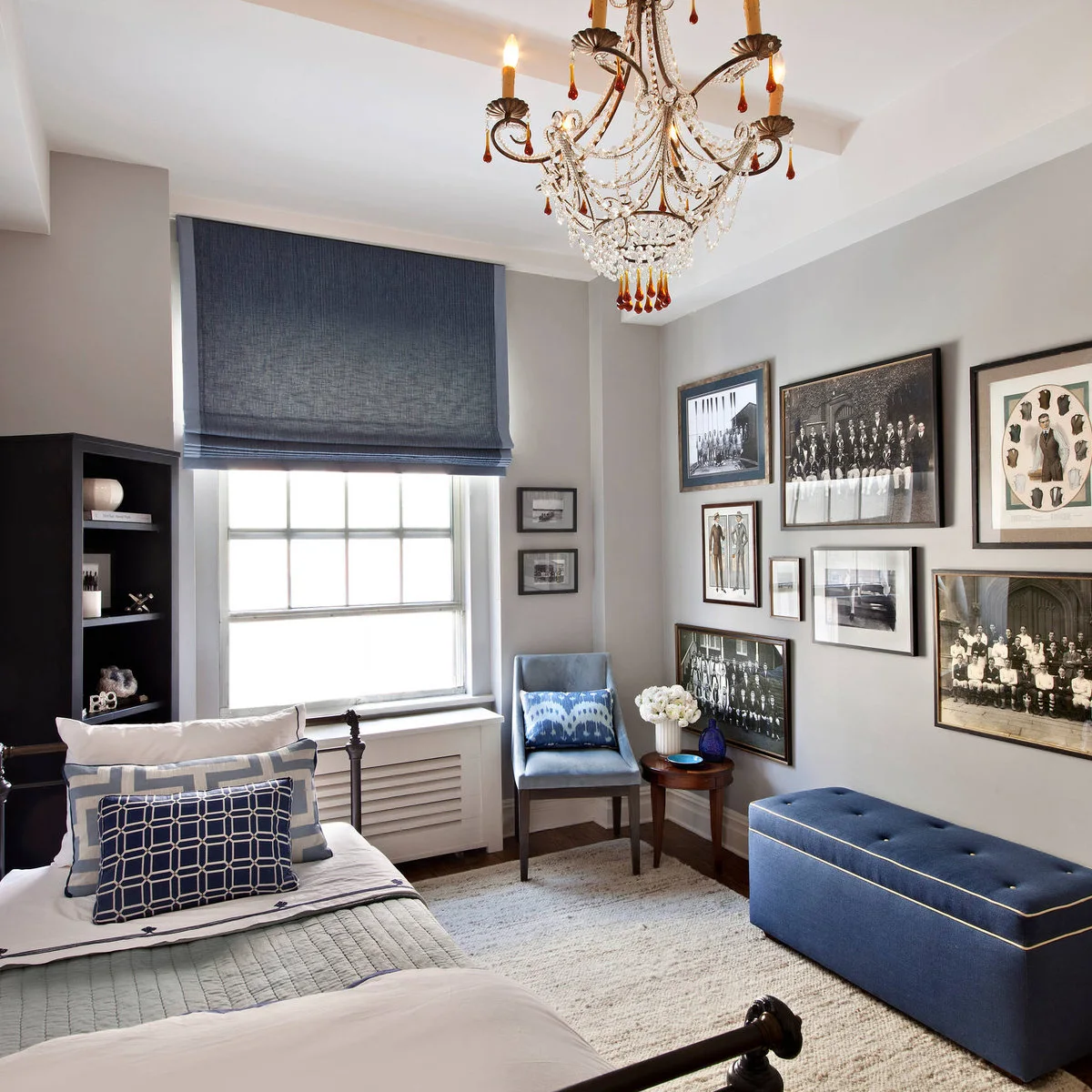 Bedroom with a gallery of old group photographs, blue seat and decorative chandelier
