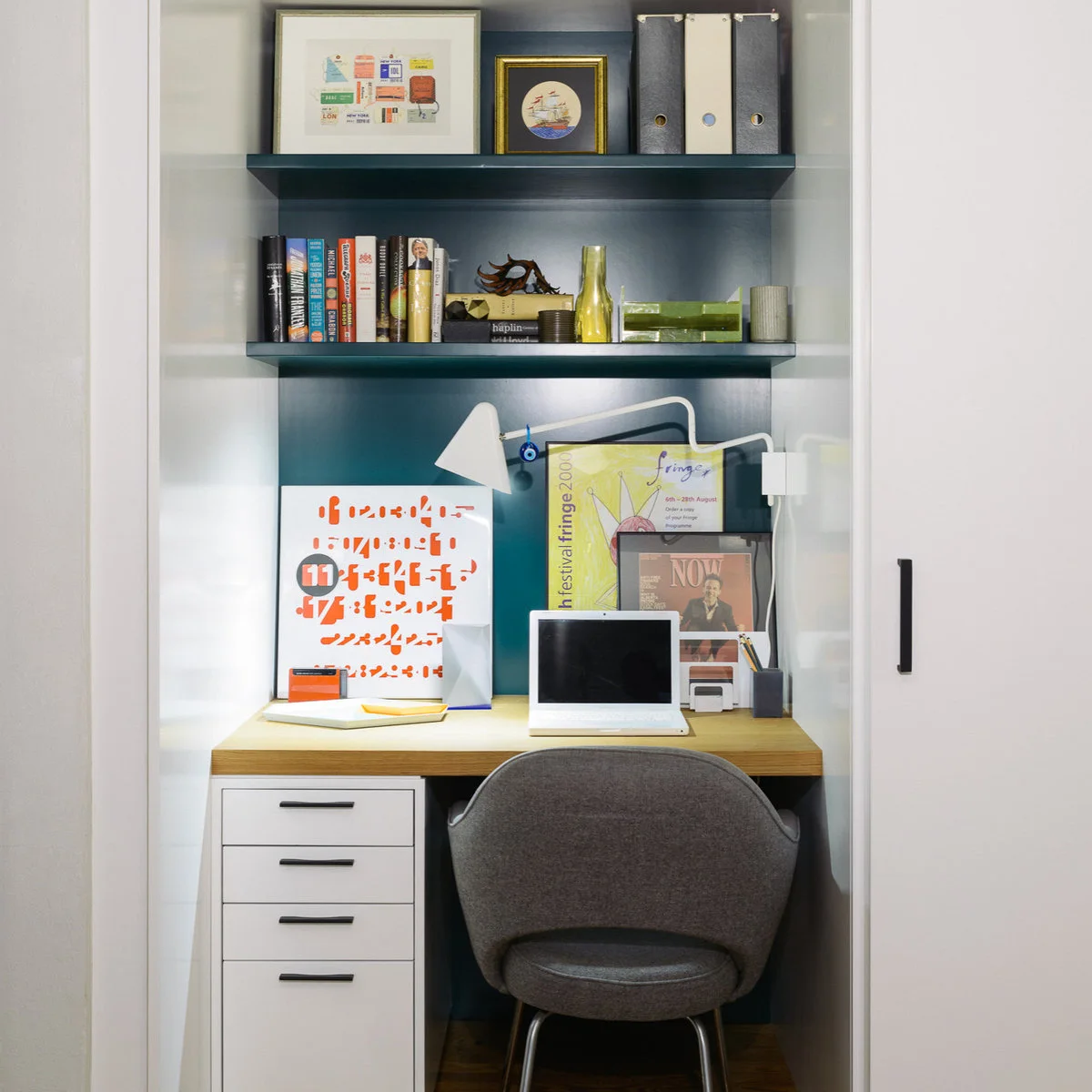 Compact wood-top desk with one white drawer unit, dark-backed shelves and a gray chair