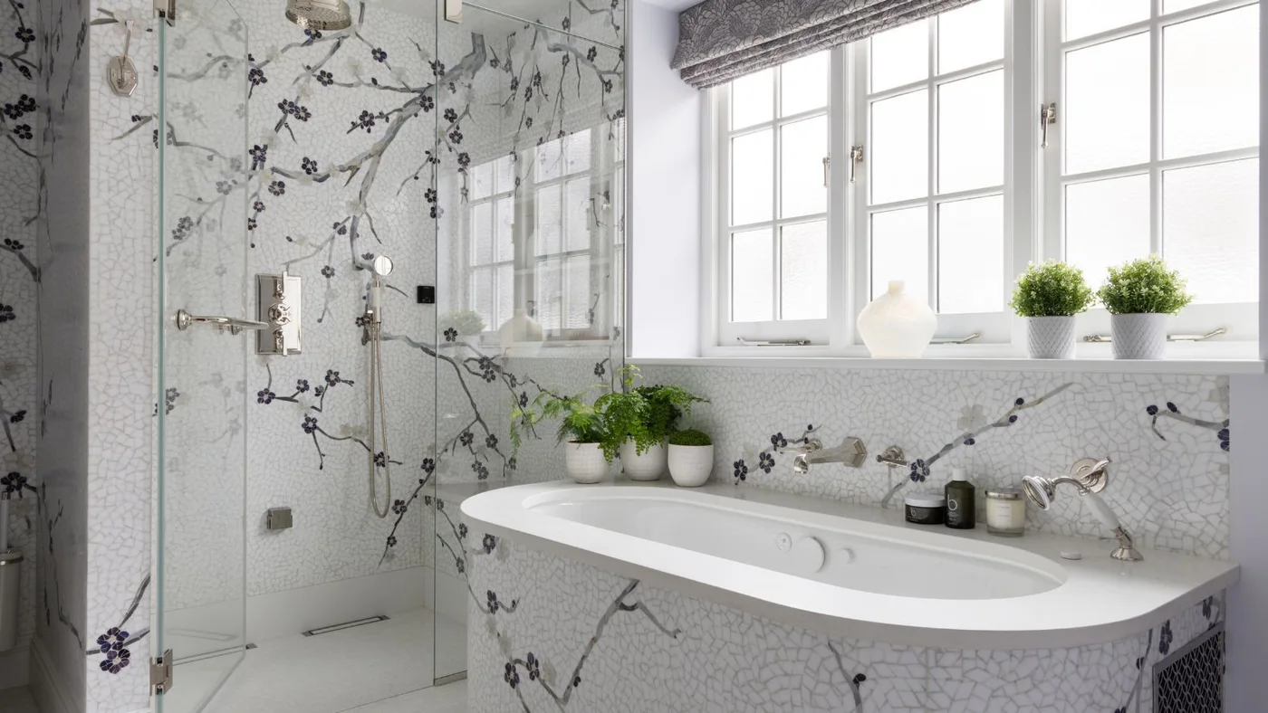 Small pale mosaic pieces form dark flowering branches across a bathroom wall and the front of a white tub.