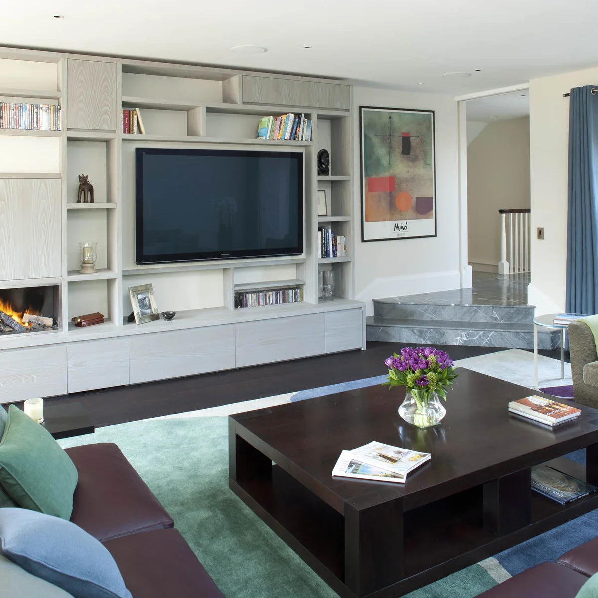 Books in an open compartment above a television within an asymmetric gray wood media unit.