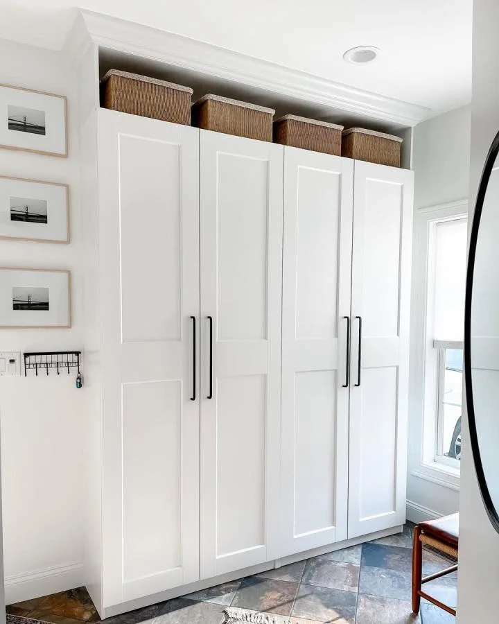 White paneled wardrobe doors with long black handles and woven baskets in a top recess in a bright entryway.