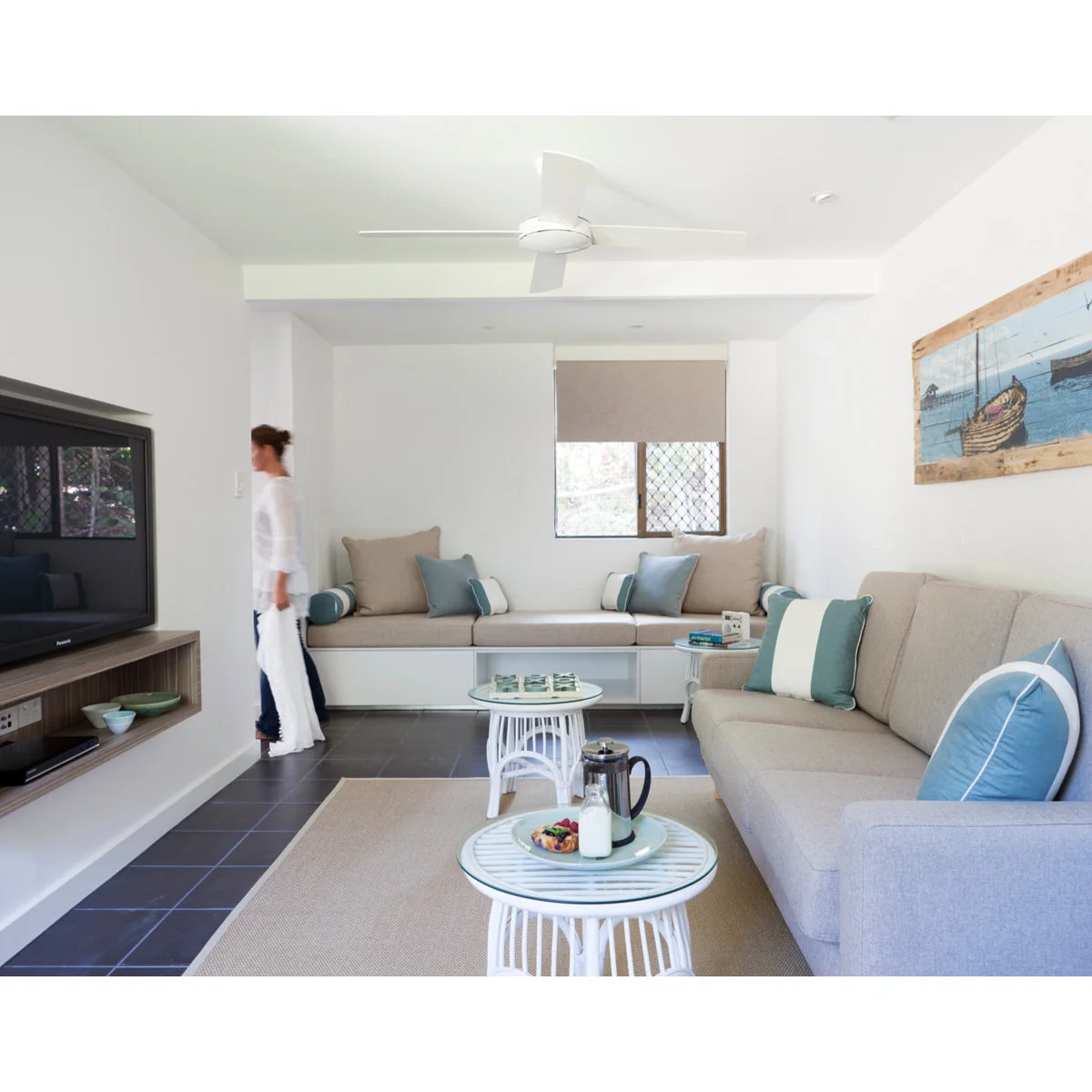 Narrow white living room with a sofa, built-in window bench and two small round tables