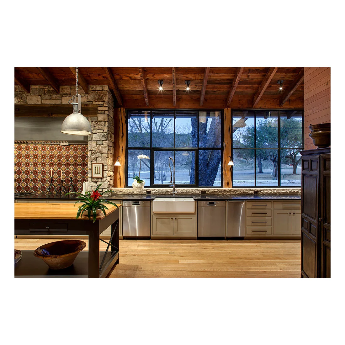A patterned tile cooking wall and stone surround beside a broad kitchen window and apron front sink