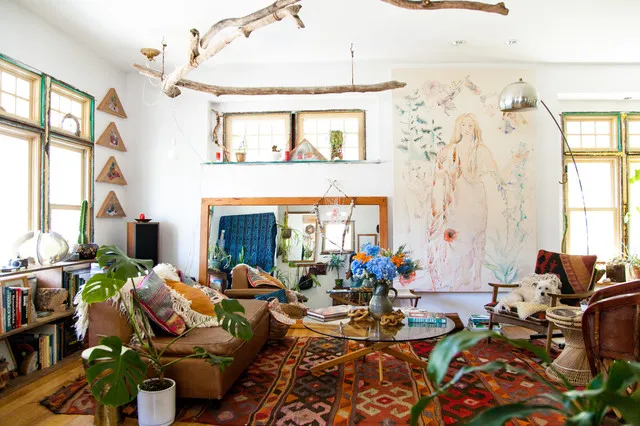 Plants gather among warm seating, patterned rugs and timber furniture beneath bright windows.