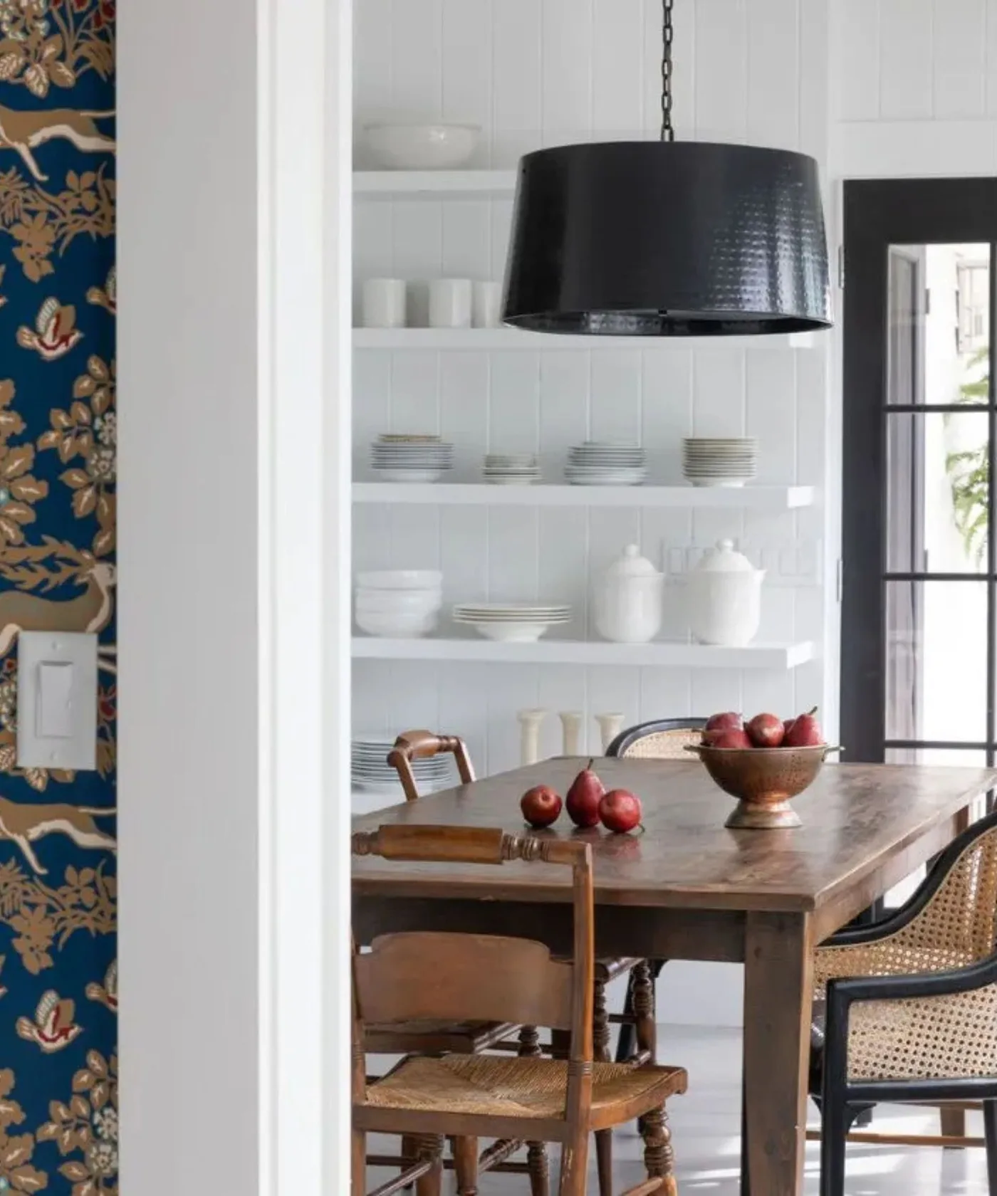 Small dining area with white open plate shelves, a wooden table, turned wooden chairs and a dark pendant shade.