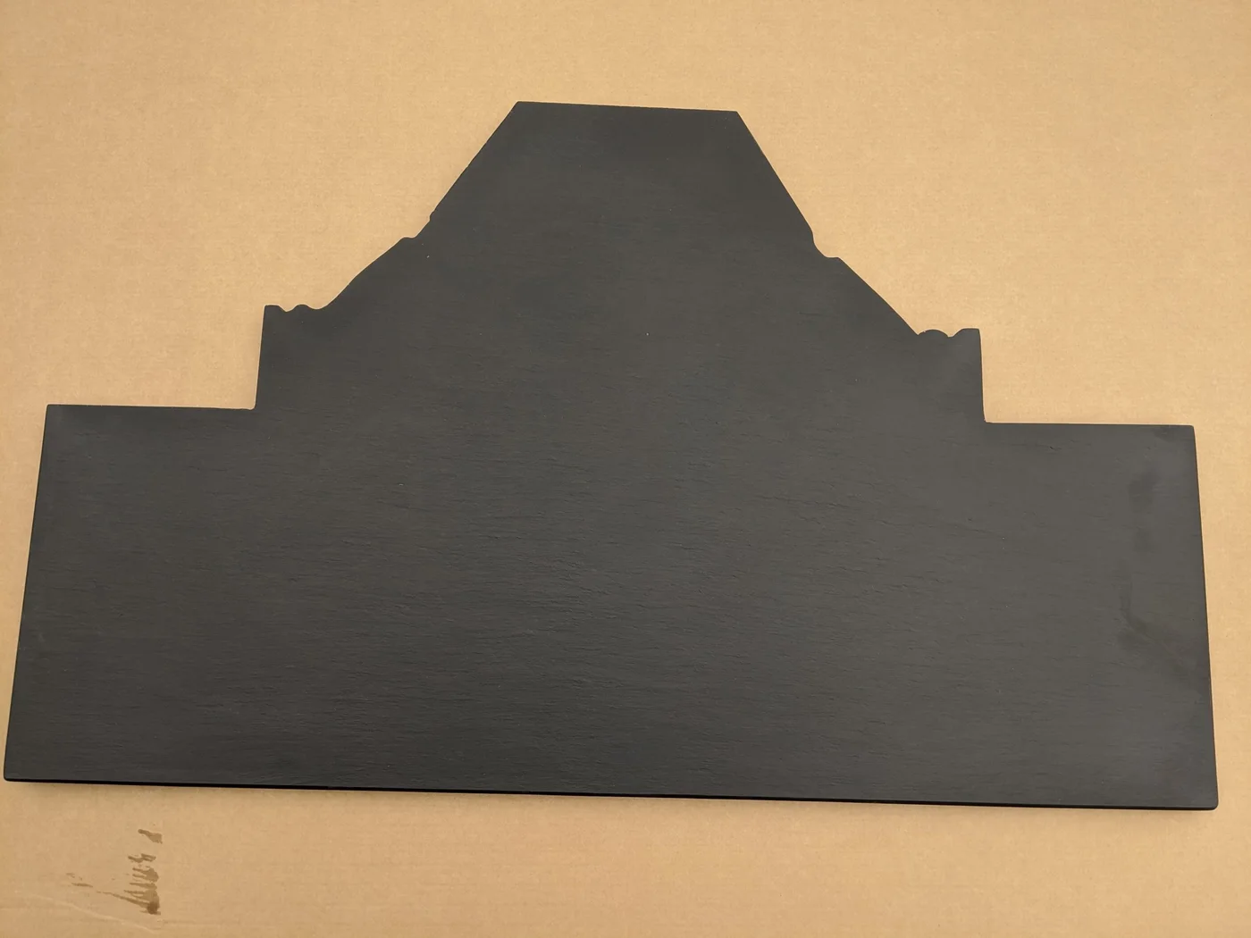 A bespoke T-shaped slate hearth lies flat in a workshop with stepped and angled cuts along its rear outline.