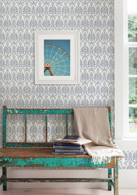 An aged green bench sits beneath a framed picture against a pale patterned wall.