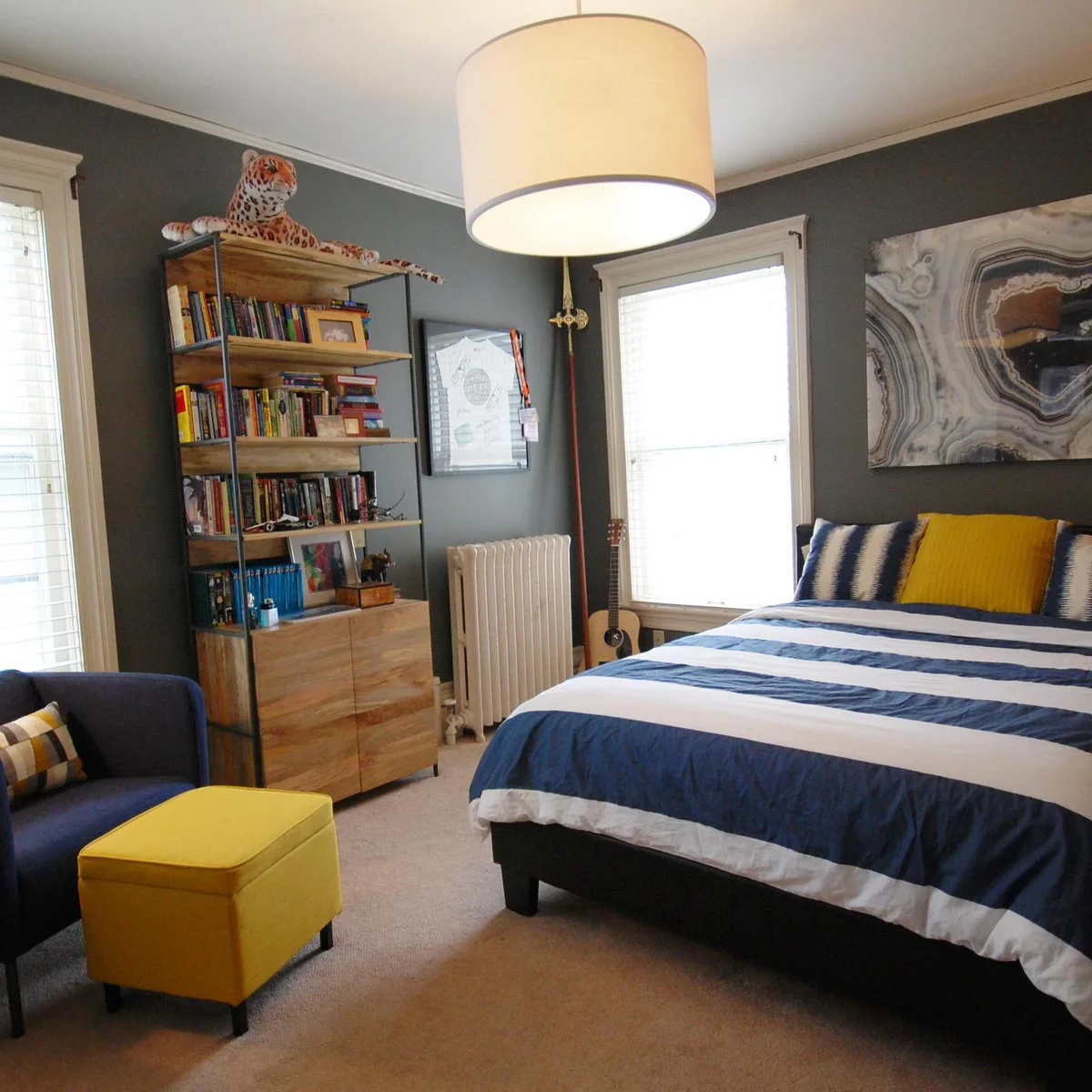 Gray teen bedroom with blue striped bedding, a dark chair and a yellow ottoman