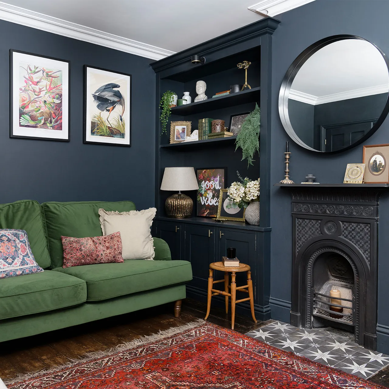 A green sofa sits beside dark built-in shelves and a fireplace above a patterned red rug