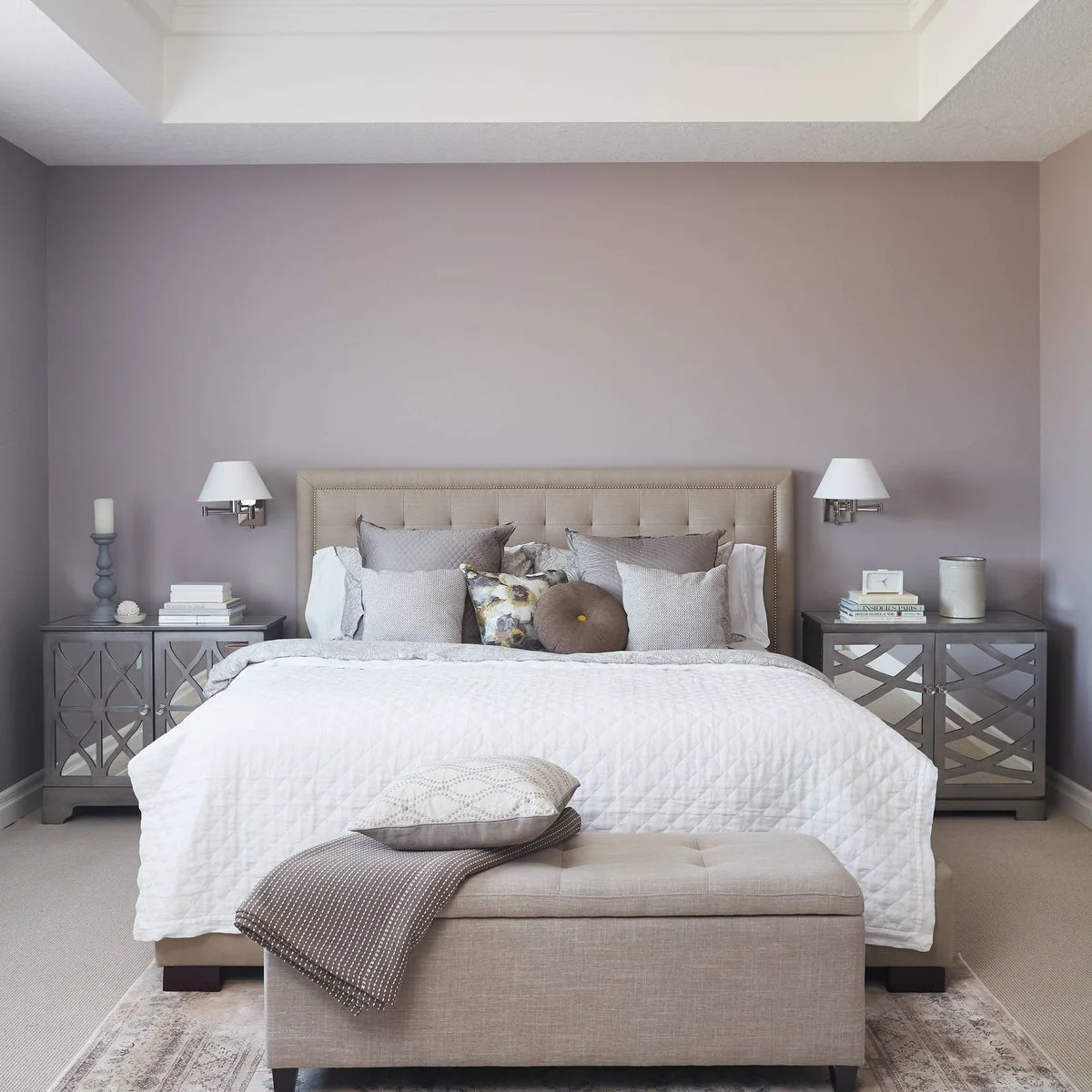 Rectangular pale upholstered bench in front of a white bed and lavender wall