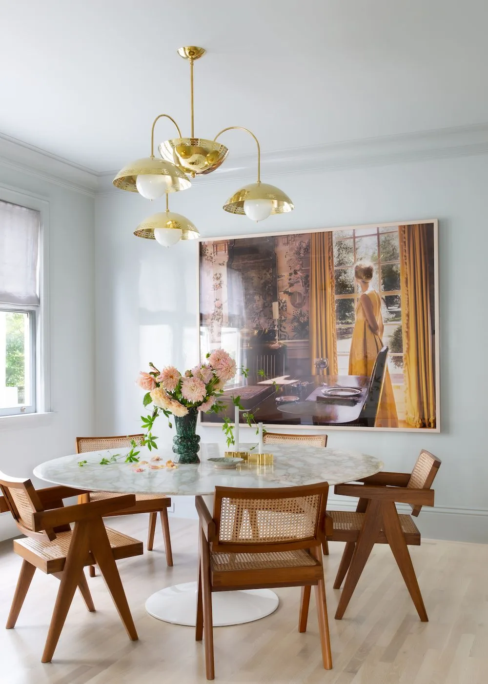 Gold-toned multi-arm fixture with pale globes above a round pale table and woven-back wood chairs