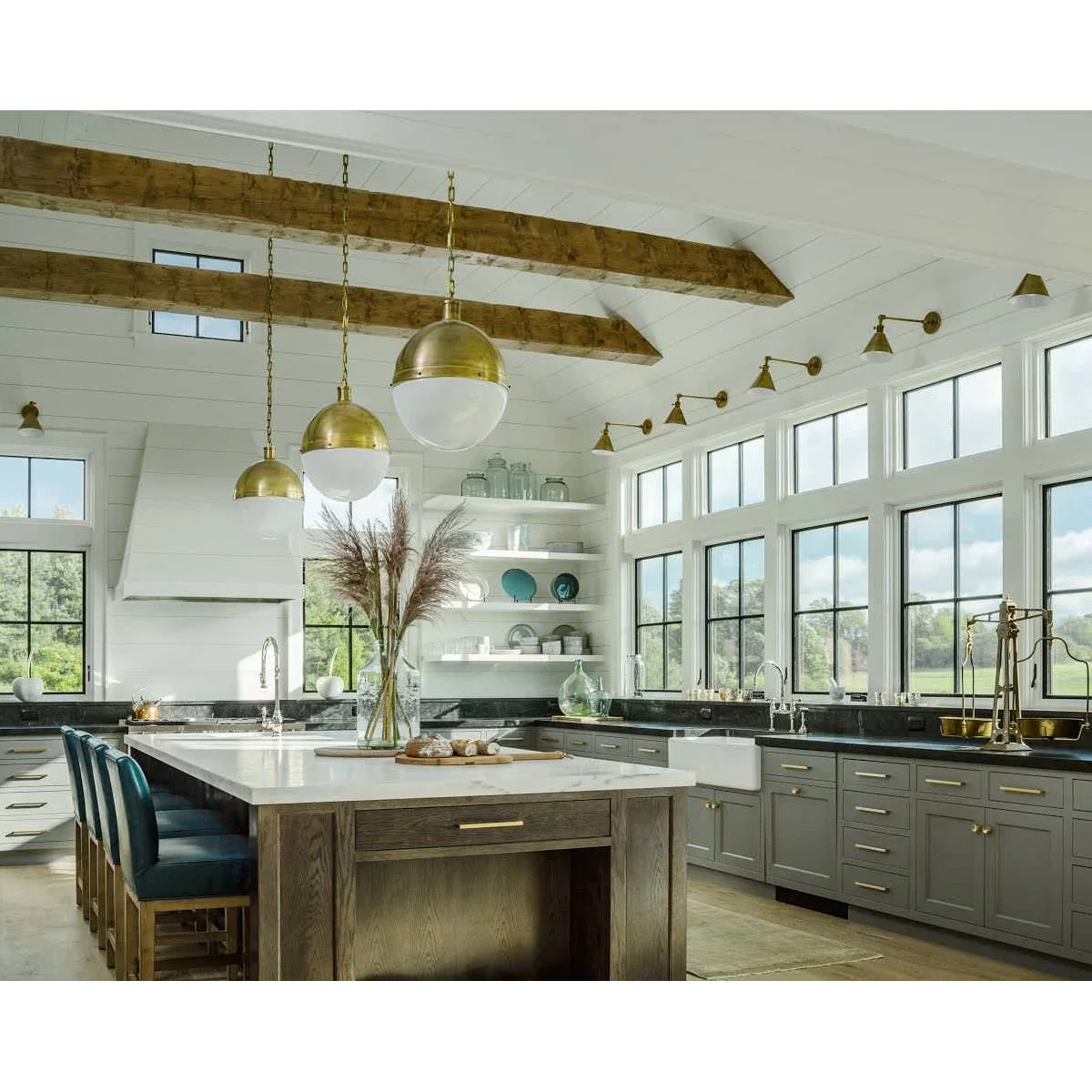 A row of small warm-metal sconces above kitchen windows with high transom panes and a long sink counter.