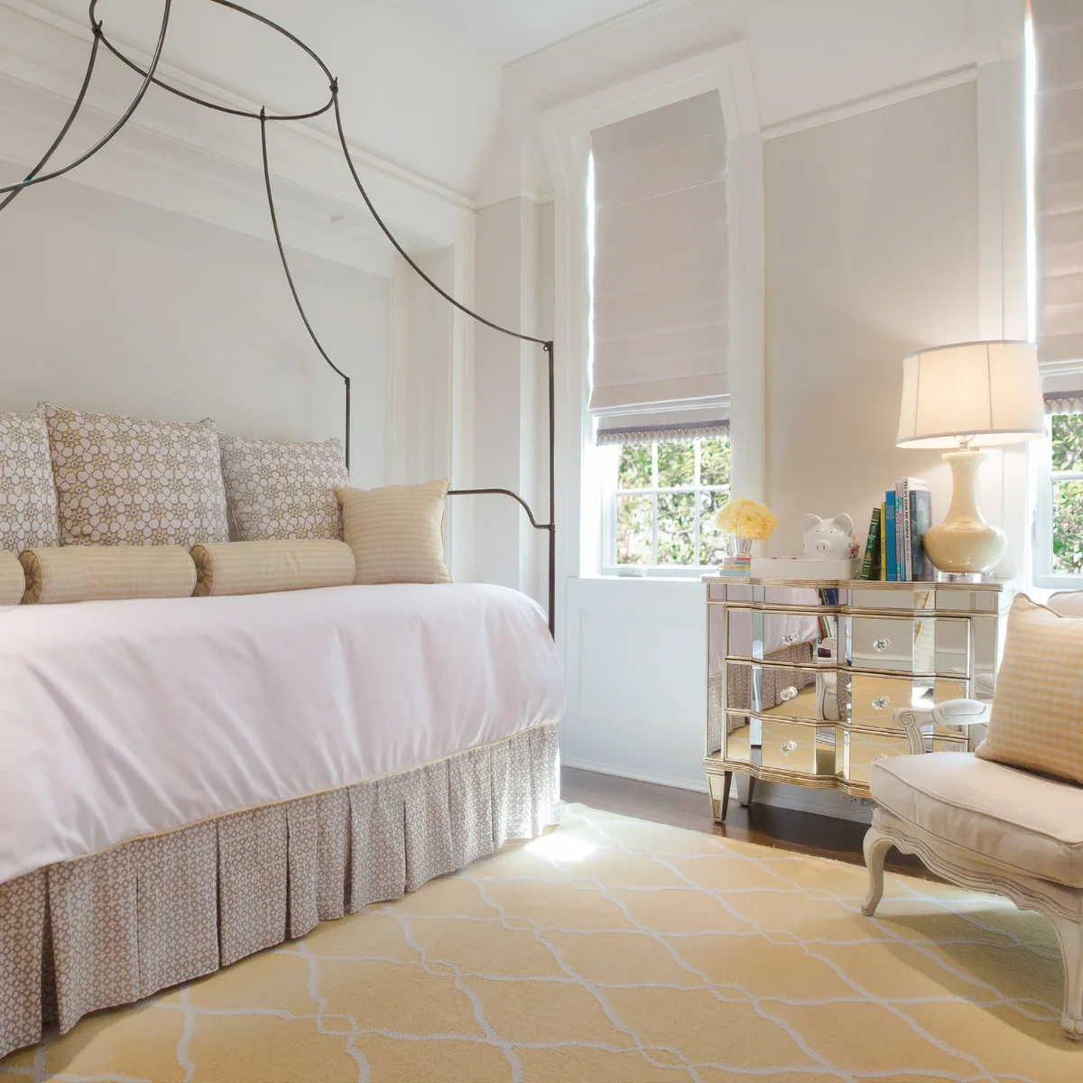 A slender dark canopy-style daybed is dressed in white bedding with pale patterned cushions and a matching bed skirt.