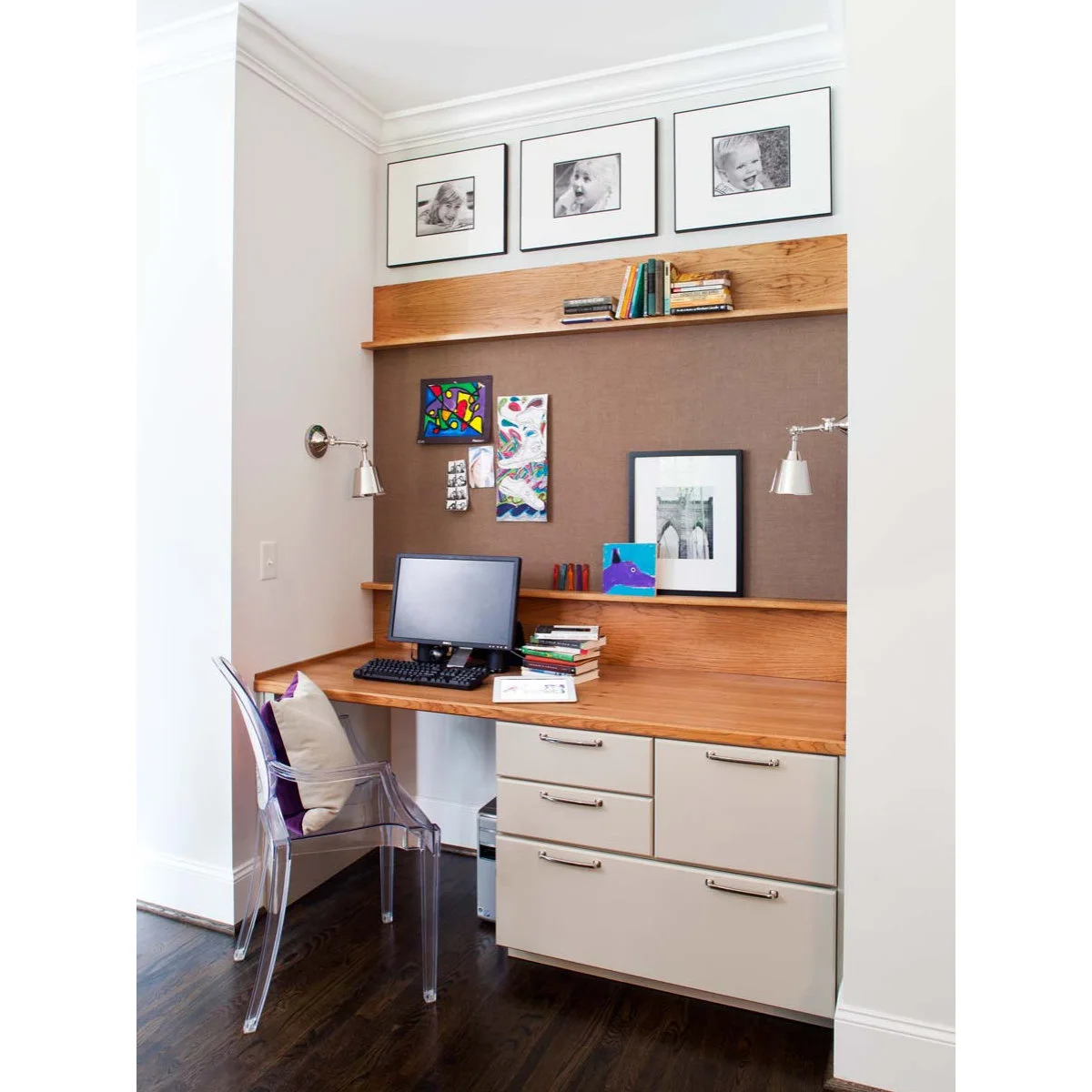 Wood-topped desk with drawers, two wall lights and a large pinboard beneath framed photographs