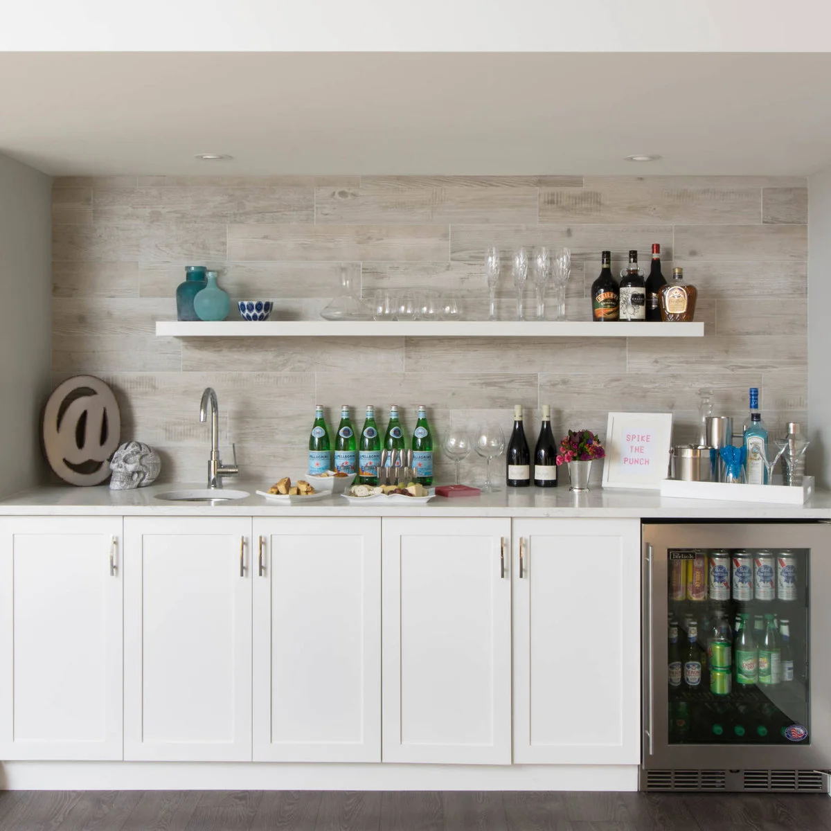 White basement wet bar with round sink, one open shelf and a beverage refrigerator