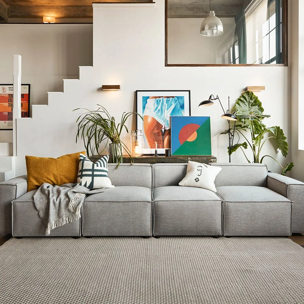 A low gray modular sofa with mustard and graphic cushions sits below colorful artwork, plants and a large wall mirror