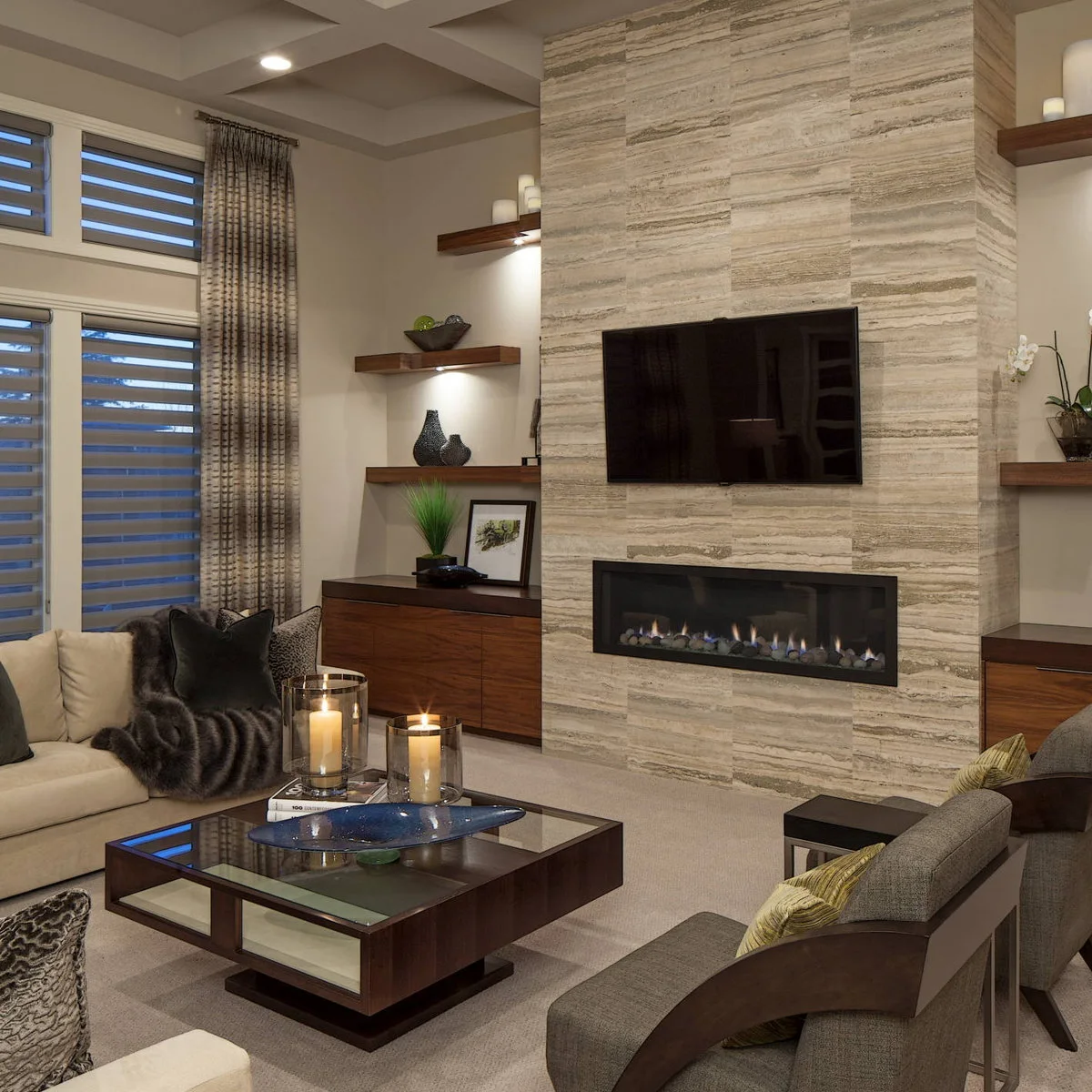 A pale sofa faces gray wood-frame chairs across a glass-topped table beside a stone fireplace and television.