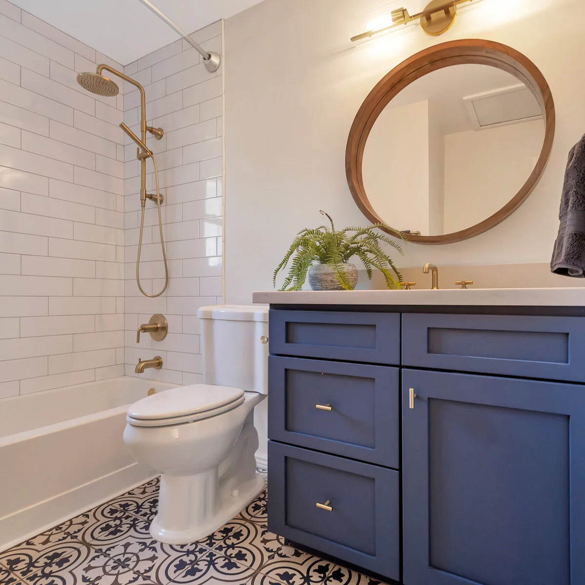 Small bathroom with a navy vanity, patterned floor, white tub and gold-colored shower fittings