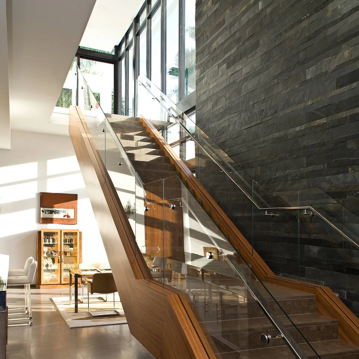 Dark horizontal wall cladding sits beside a glass-sided staircase and tall windows.