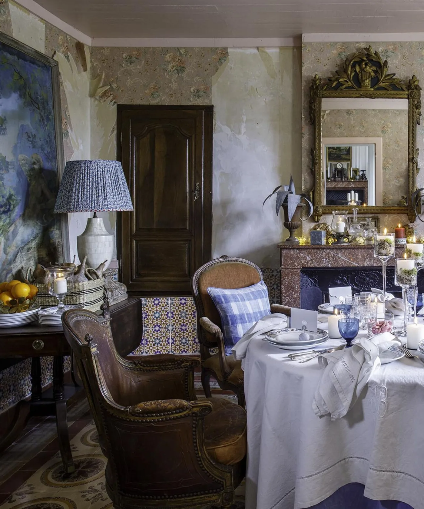 Cloth-covered dining table with ornate wooden chairs, blue glassware, patterned walls and a large framed mirror.
