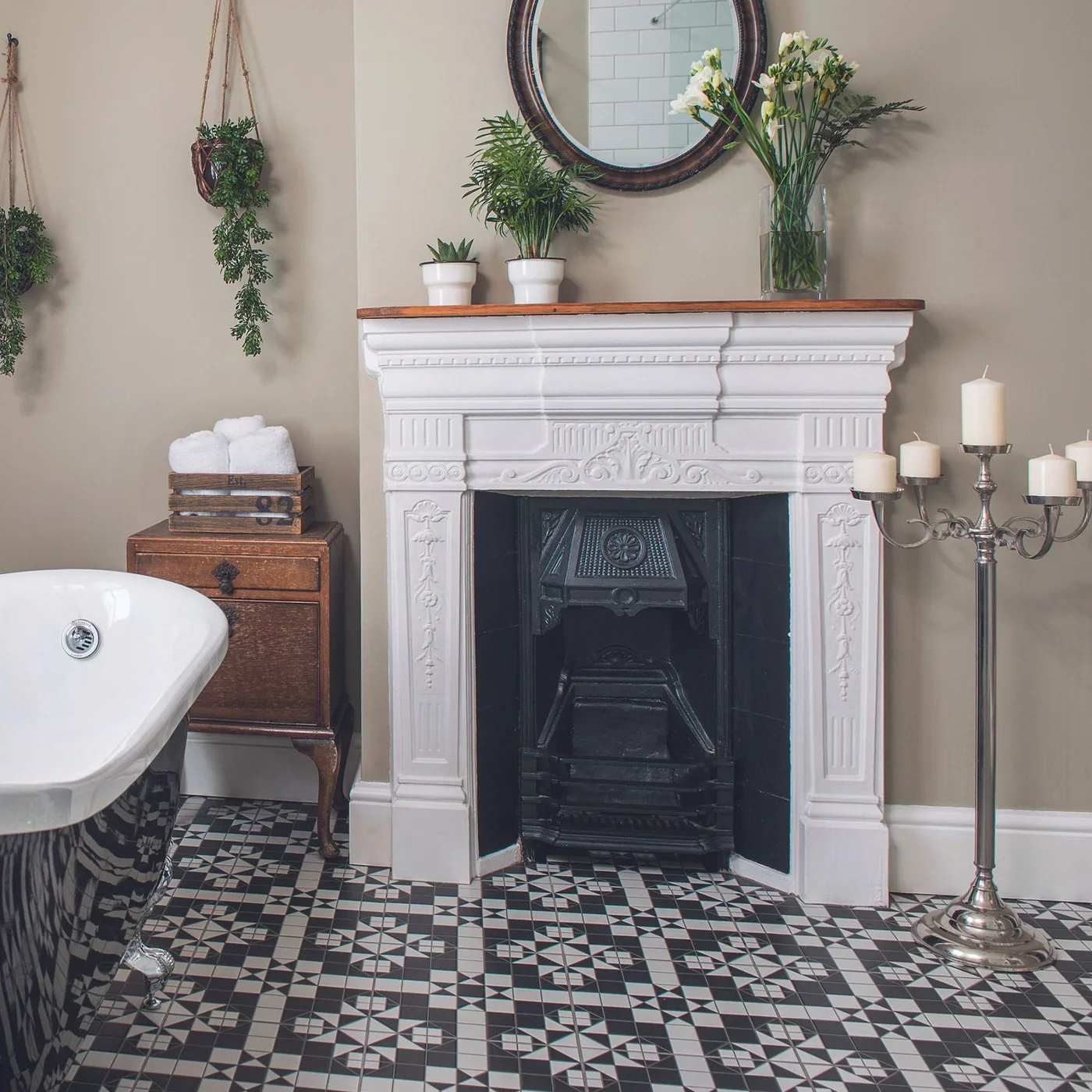 A white ornate fireplace with a dark insert stands beside a bath and timber storage above a patterned floor.