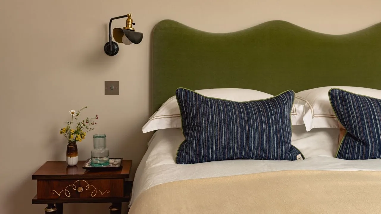 Sand-colored bedroom wall behind an olive headboard, white bedding and blue striped cushions.