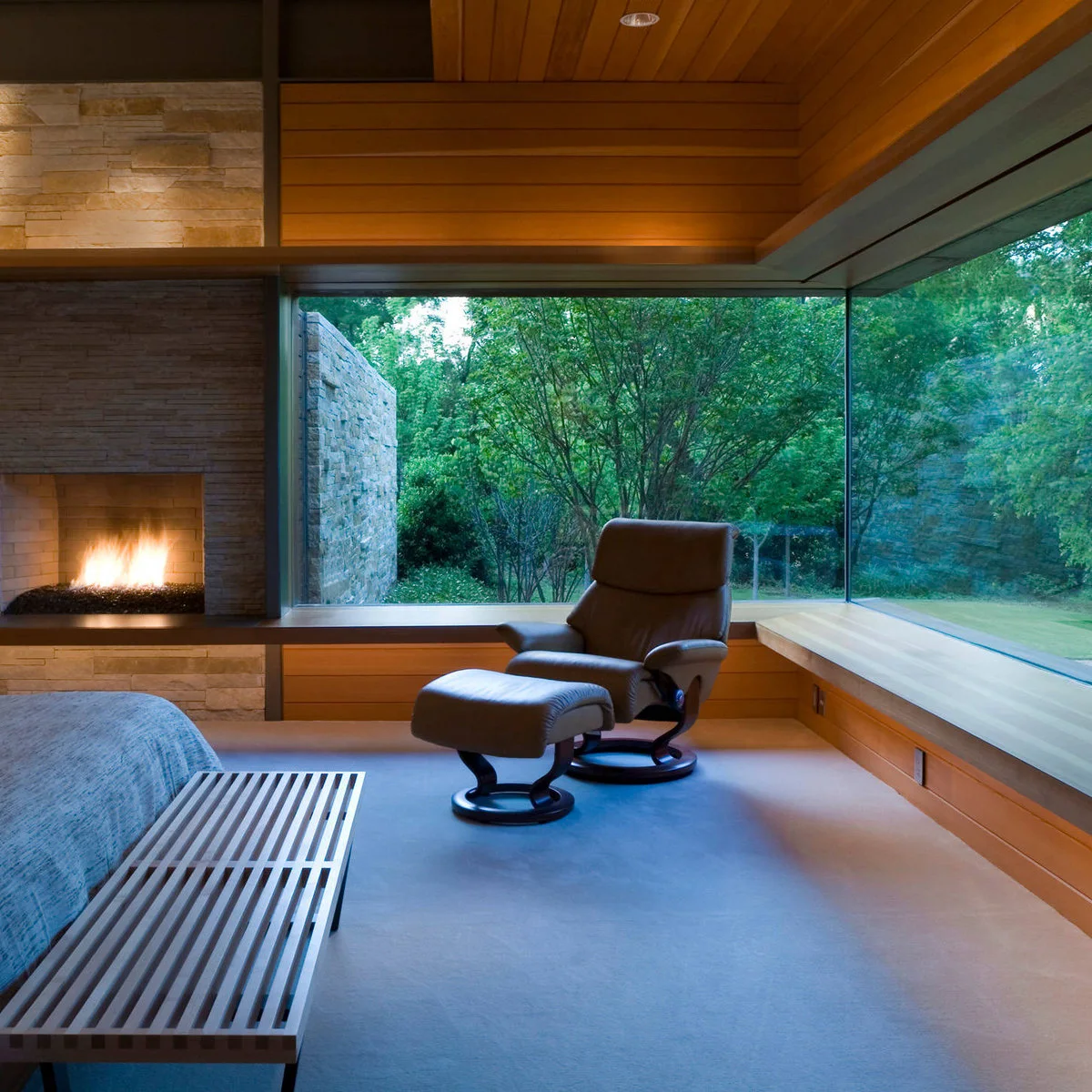 Slatted bench at the foot of a bed in a wood-toned bedroom overlooking trees