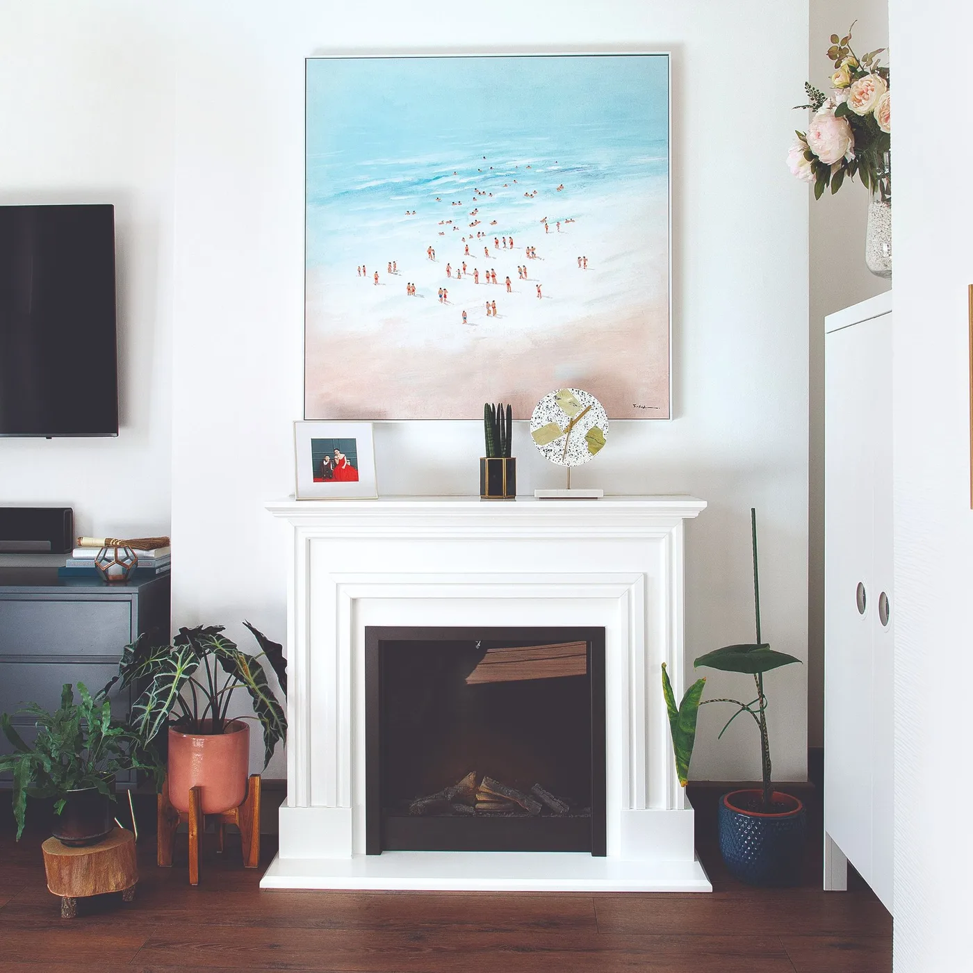 White fireplace below large beach picture with small mantel objects and plants on either side